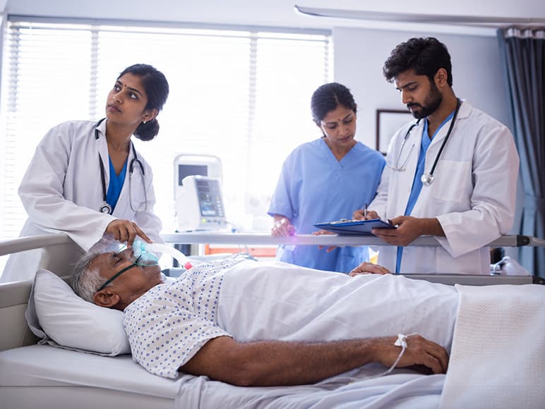 Doctors and a nurse caring for an older patient on oxygen in a hospital bed
